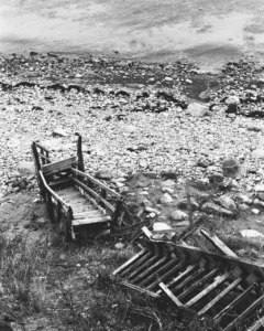 A broken staircase leading down to a stone covered beach.